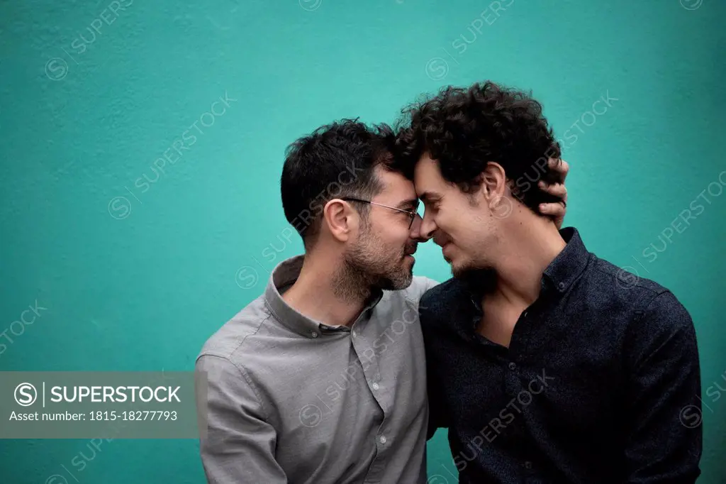 Gay couple romancing in front of Turquoise wall