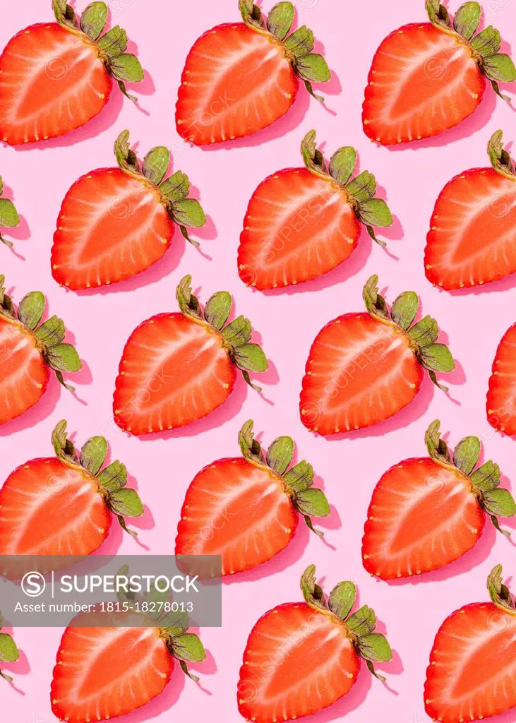 Pattern of rows of fresh halved strawberries lying against pink background