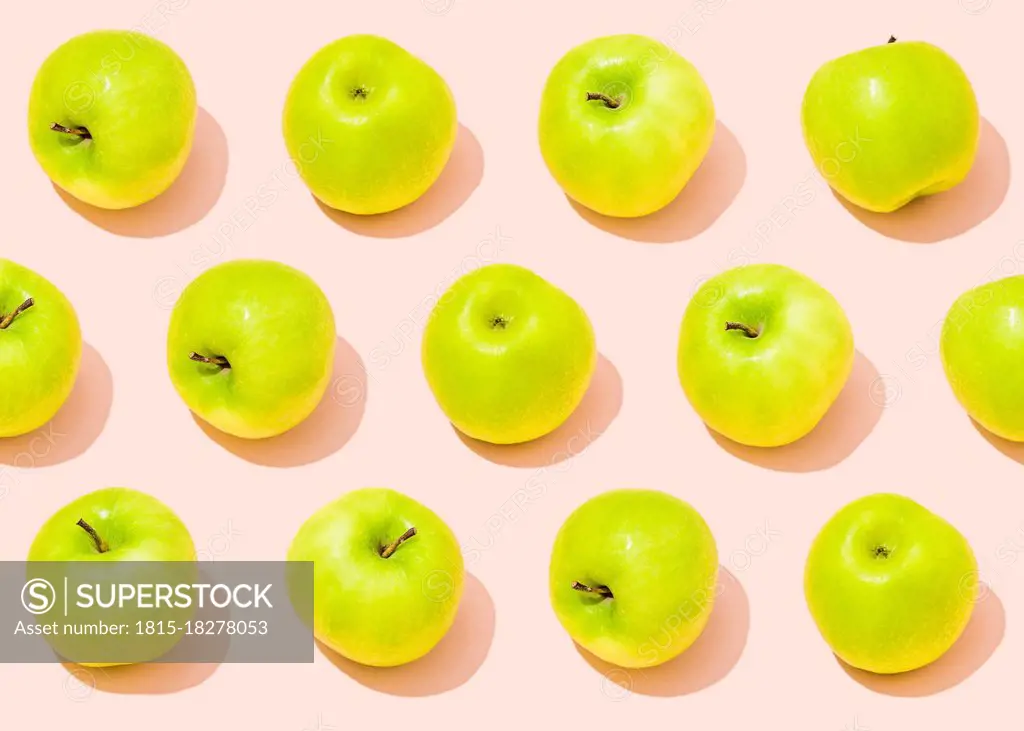 Pattern of green apples lying against light pink background