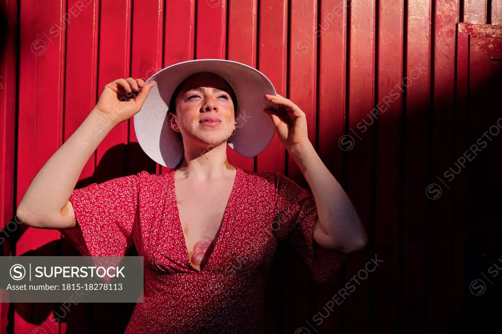 Young woman looking away wearing sun hat by red wall