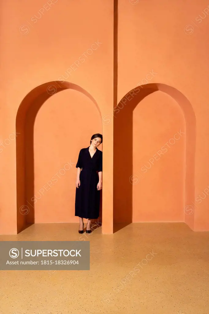 Trapped young woman leaning on arch over orange wall