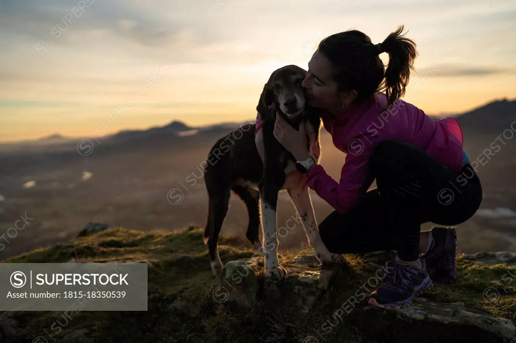 Woman kissing dog while kneeling on hill