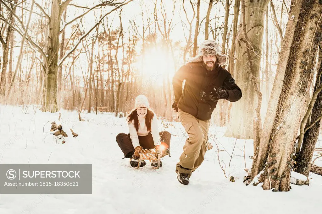 Playful man pulling woman sitting on sled in forest