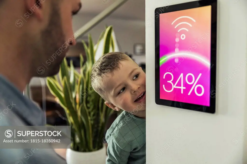 Smiling boy with father looking at smart thermostat in home