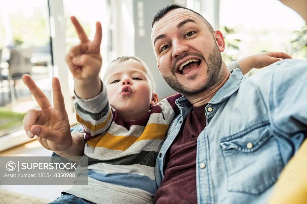 Happy father and son gesturing peace sign in living room at home