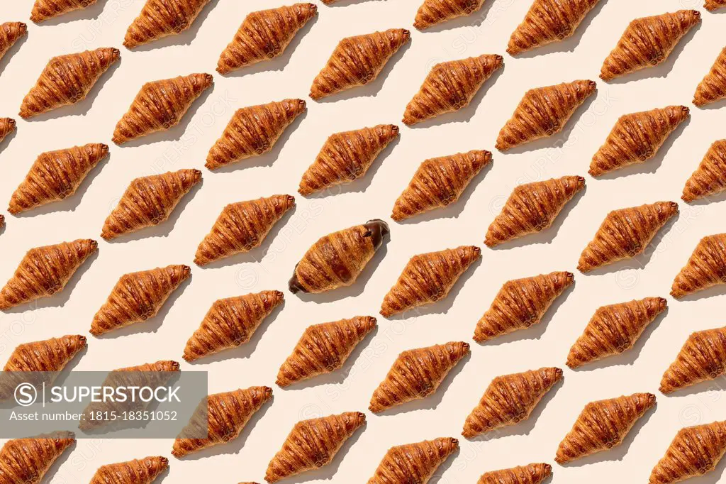 One chocolate croissant amidst butter croissants on beige background