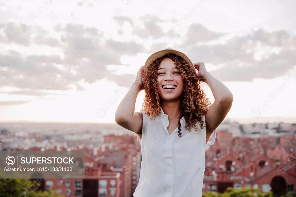 Cheerful woman smiling in front of city during sunset