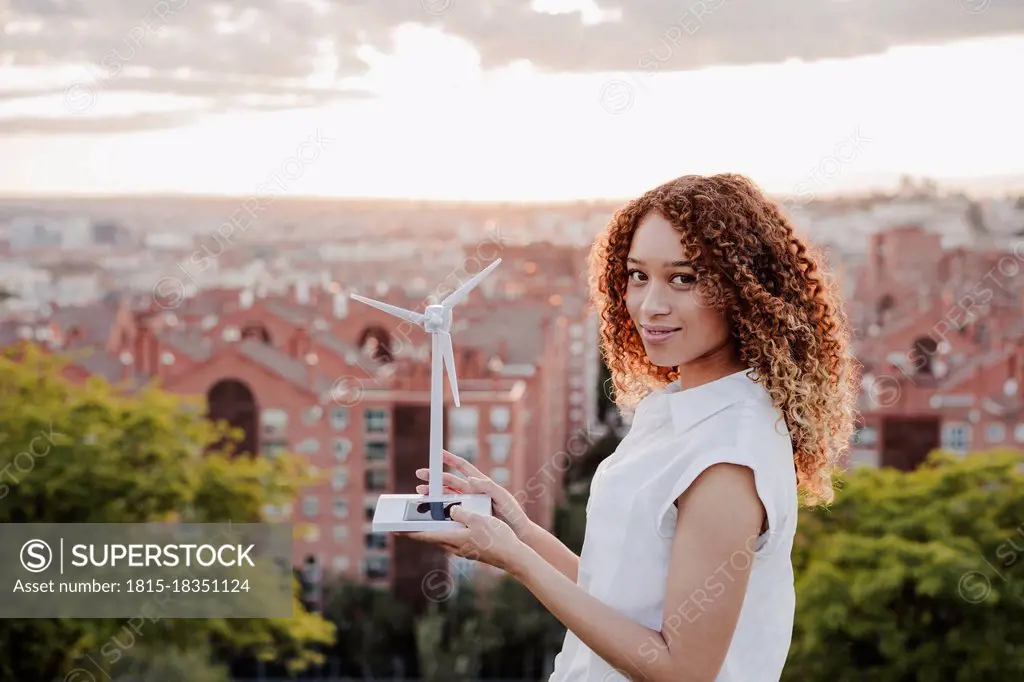 Young Hispanic woman holding wind turbine standing by city