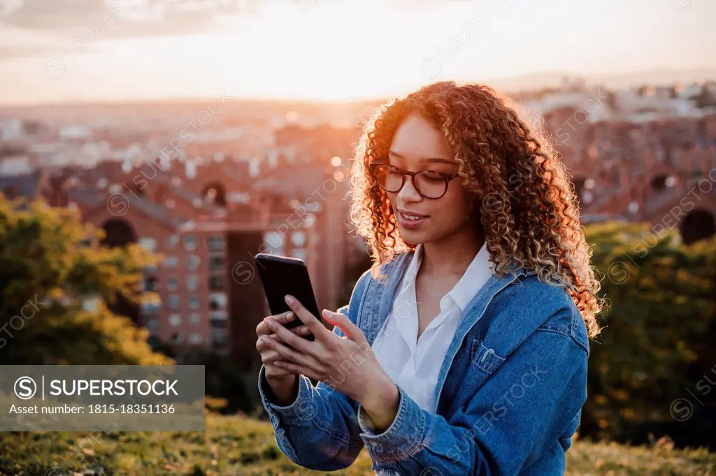 Hispanic woman text messaging on smart phone in park