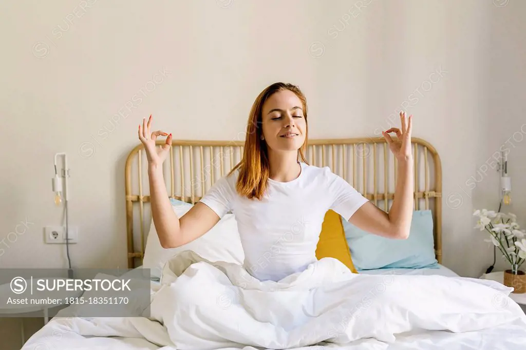 Redheaded woman meditating on bed at home