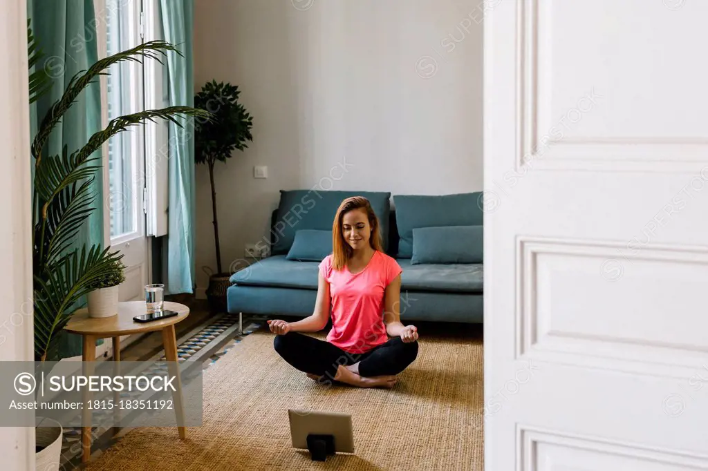 Young woman meditating in living room at home