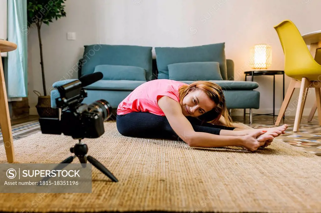 Female influencer vlogging while doing stretching exercise at home