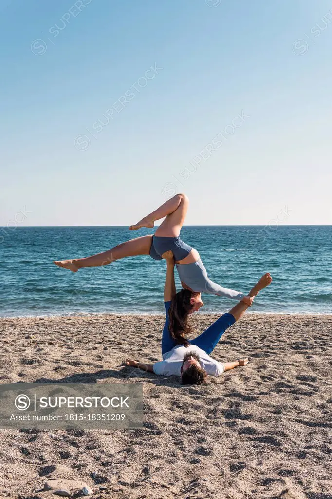 Couple doing acroyoga on the beach. Woman balancing on man