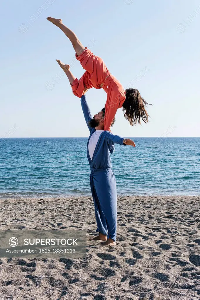 Girlfriend balancing on boyfriend shoulder while practicing acroyoga on beach