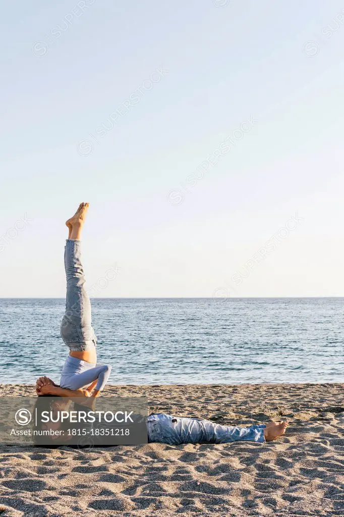 Couple kissing while practicing acroyoga on beach during sunny day