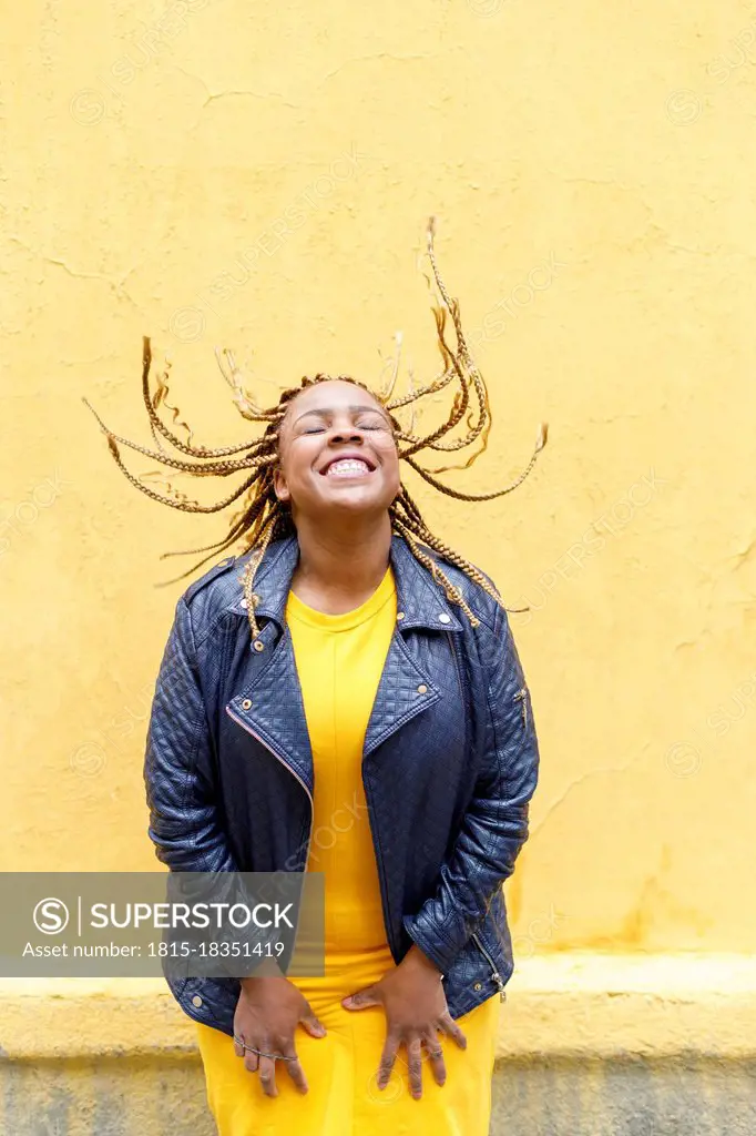 Playful plus size woman tossing braids in front of yellow wall