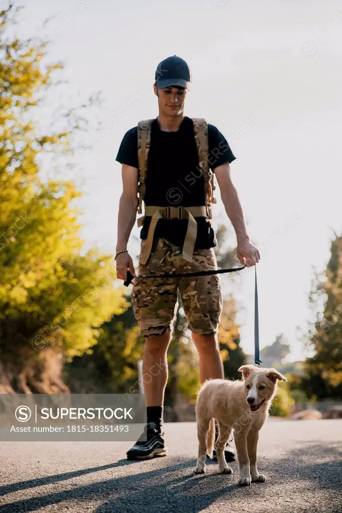 Young man with backpack standing with dog on road