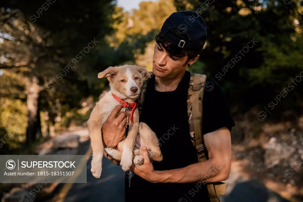 Young male hiker standing with backpack and pet in forest