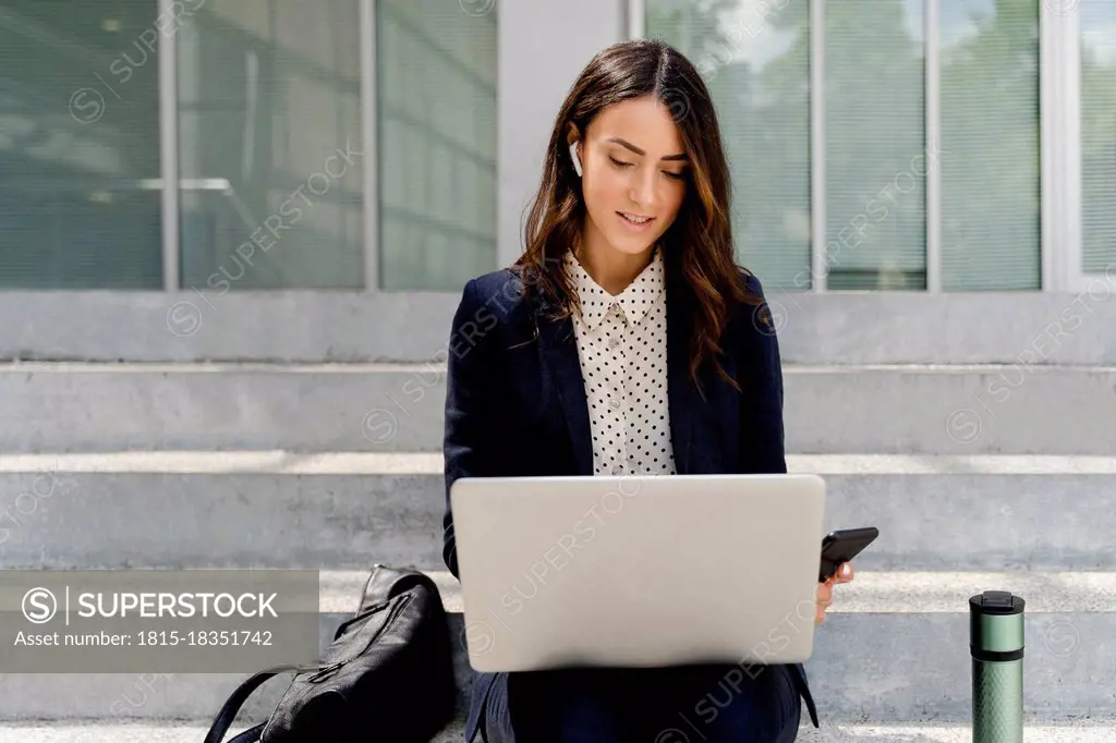 Businesswoman working on laptop while sitting on staircase