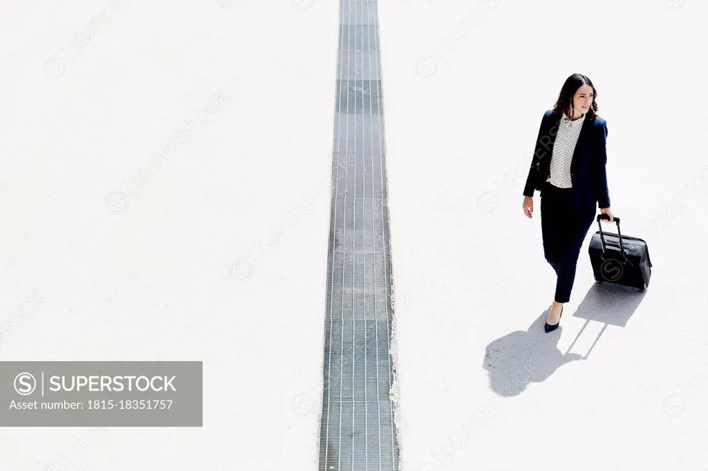 Businesswoman walking with suitcase during sunny day