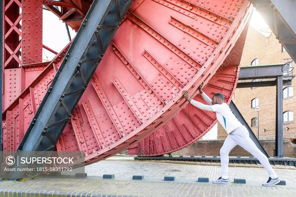 Young man stretching under red metallic structure at bridge