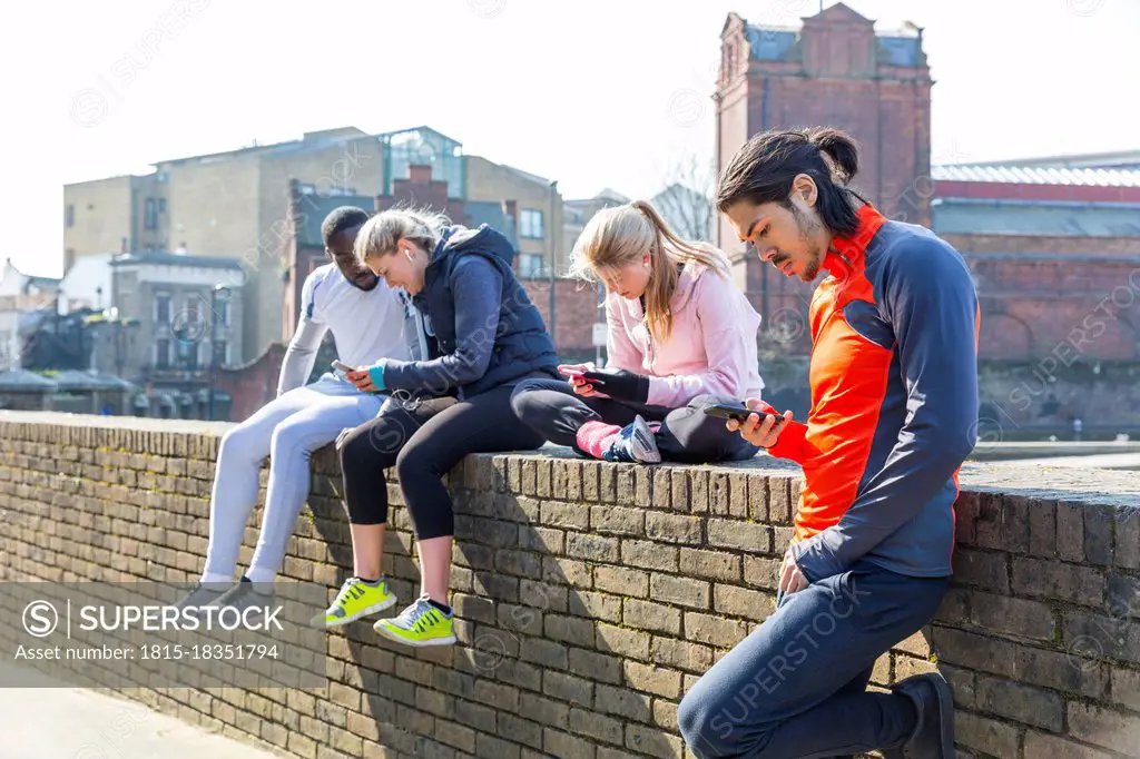 Multi-ethnic fitness friends using smart phones at wall