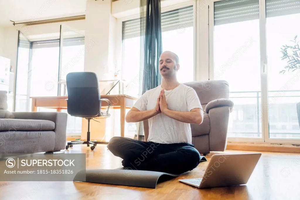 Man with hands clasped meditating while sitting on mat at home