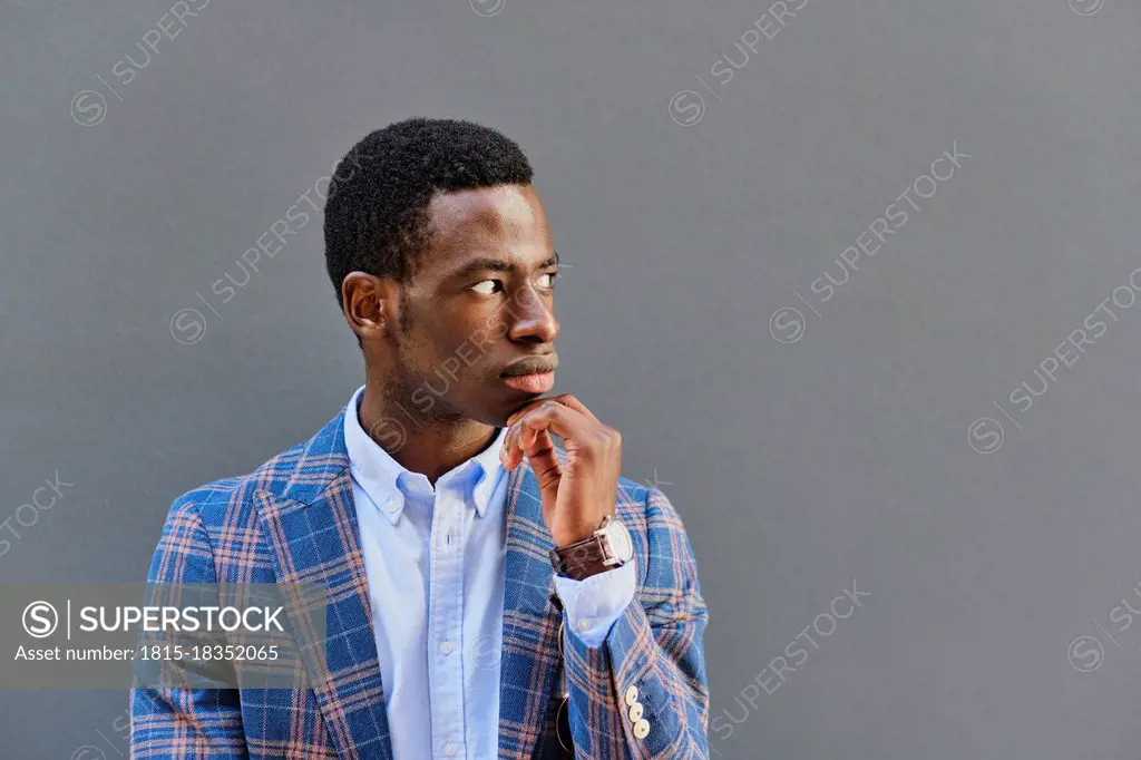 Thoughtful businessman with hand on chin looking away in front of gray wall