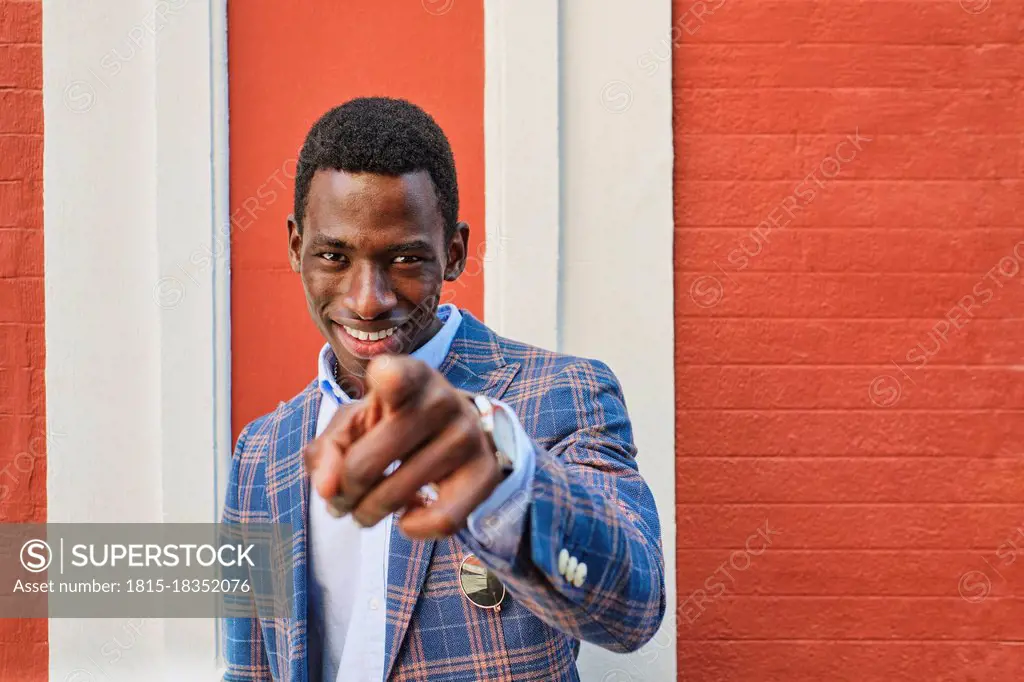 Young male entrepreneur smiling while pointing in front of wall