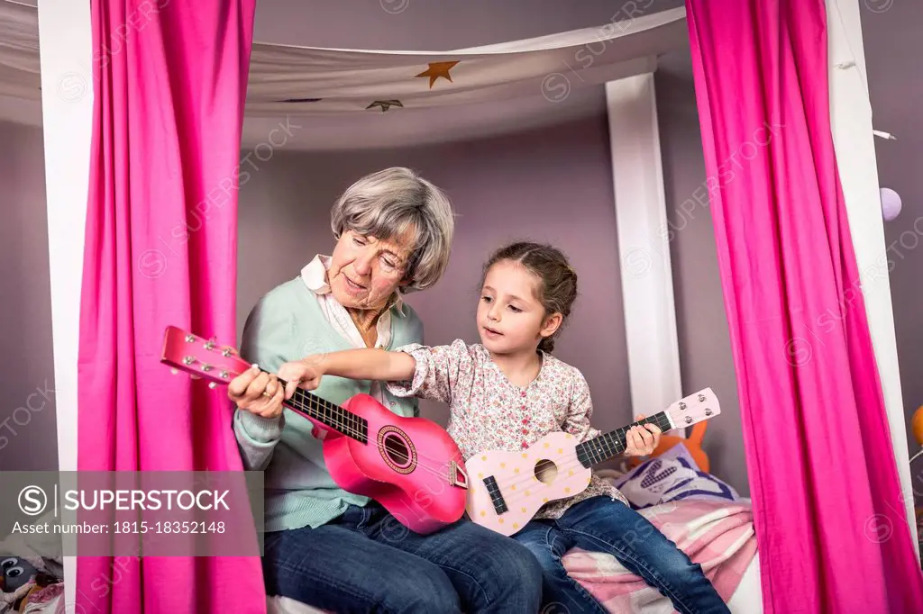 Granddaughter teaching about guitar to grandmother in bedroom