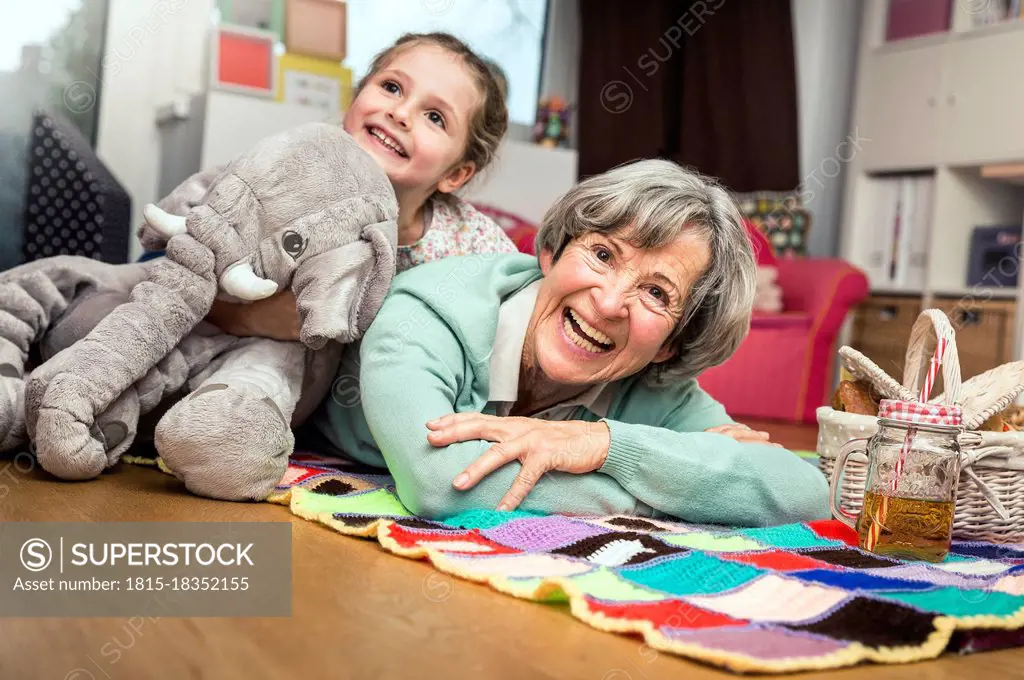 Girl leaning with toy on woman lying down in nursery