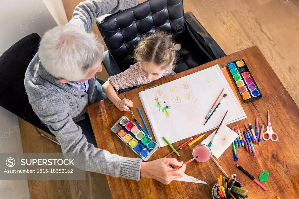 Senior man and girl painting in paper on table at home