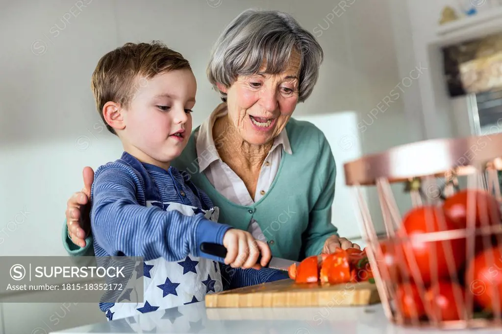 Grandson cutting tomato by grandmother in kitchen