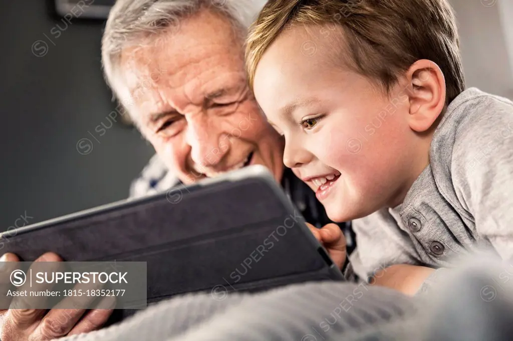 Smiling boy using digital tablet with senior man at home