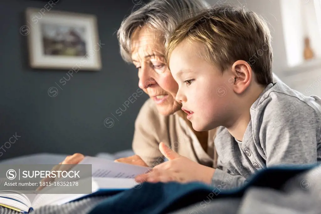 Grandmother reading book while lying by grandson in bedroom