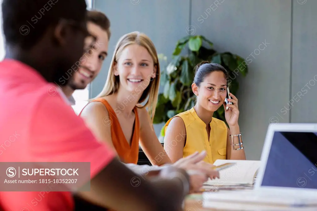 Smiling businesswoman talking on smart phone while male and female entrepreneurs discussing in meeting at office