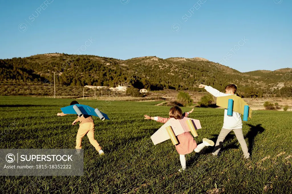 Playful brothers and sister playing with rocket wings on agricultural field during sunny day