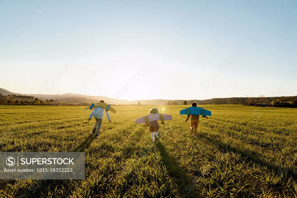 Playful brothers and sister with rocket wings running on agricultural field during sunny day