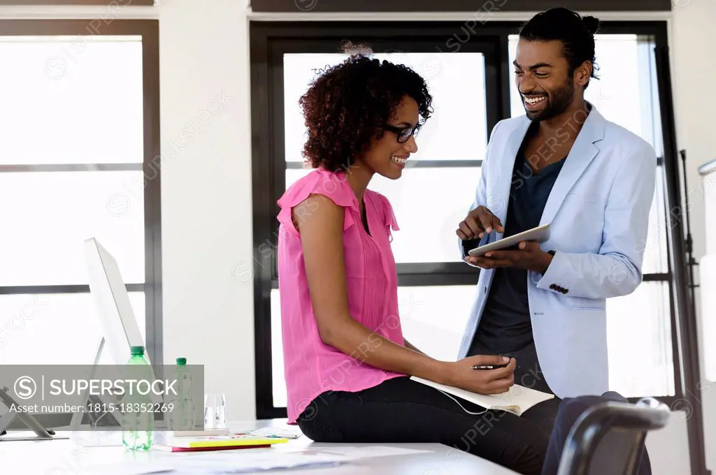 Cheerful businessman and businesswoman discussing over digital tablet in office