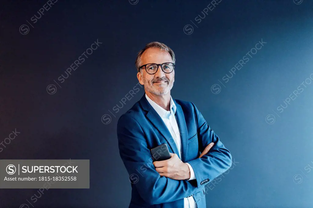 Smiling businessman with arms crossed standing in front of blue wall