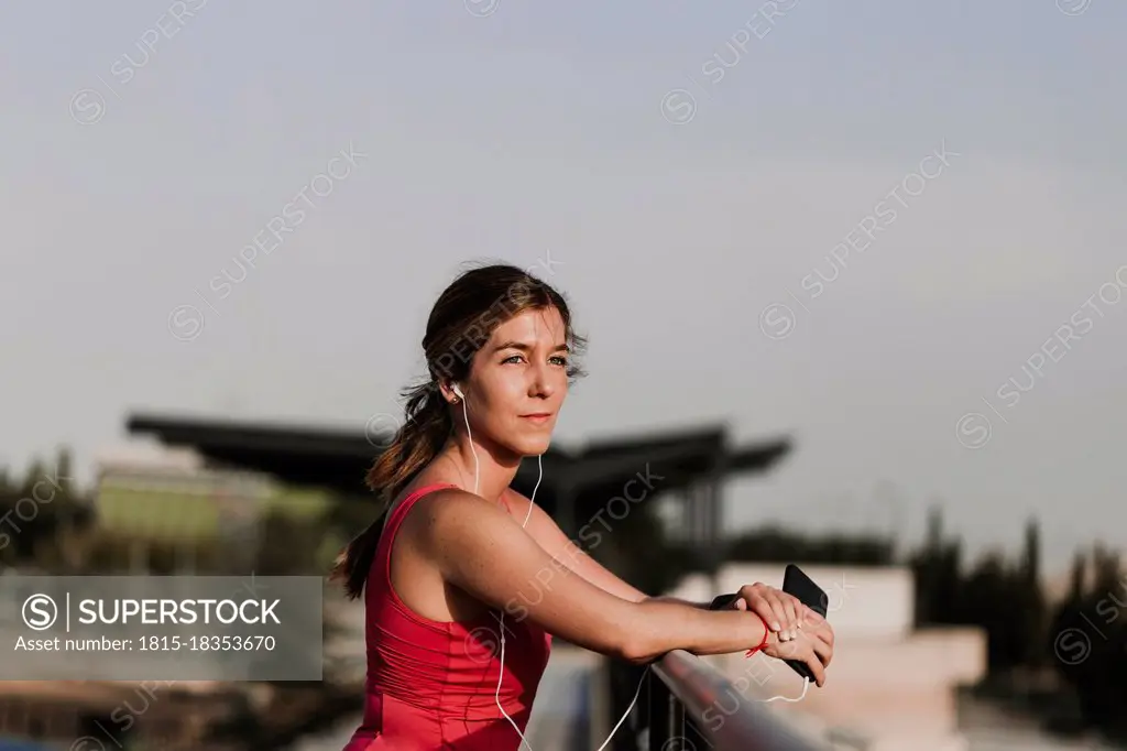 Sportswoman listening to music while leaning on railing