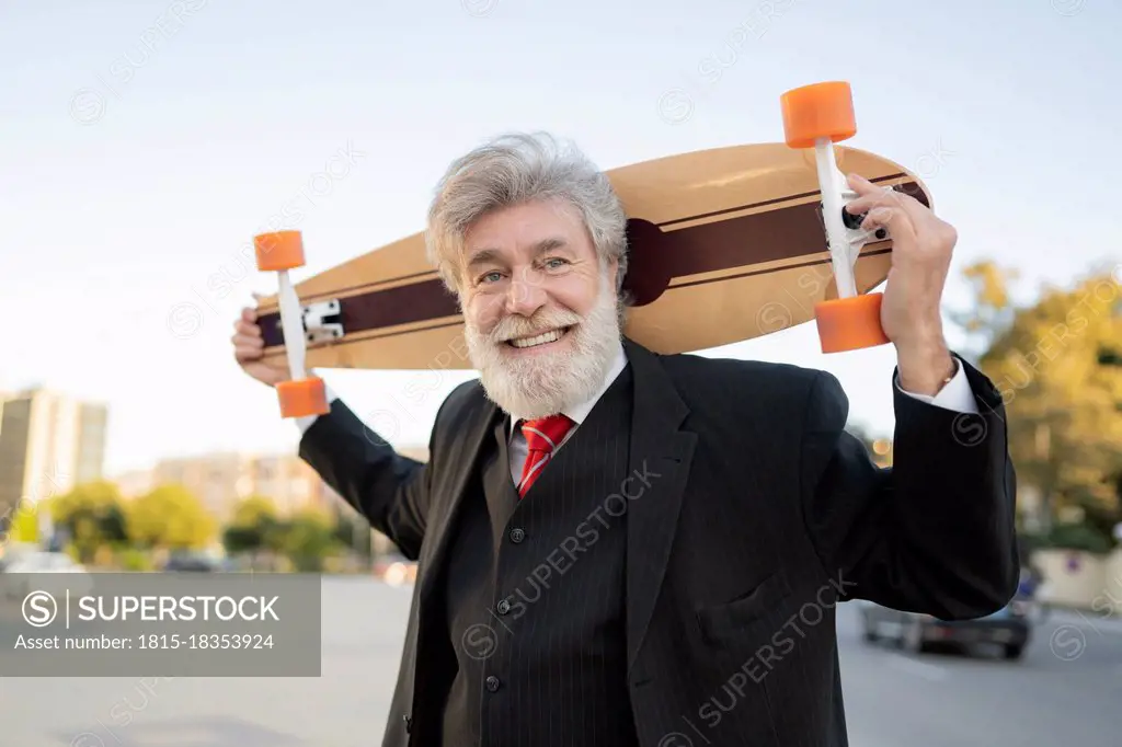 Smiling businessman carrying skateboard in city