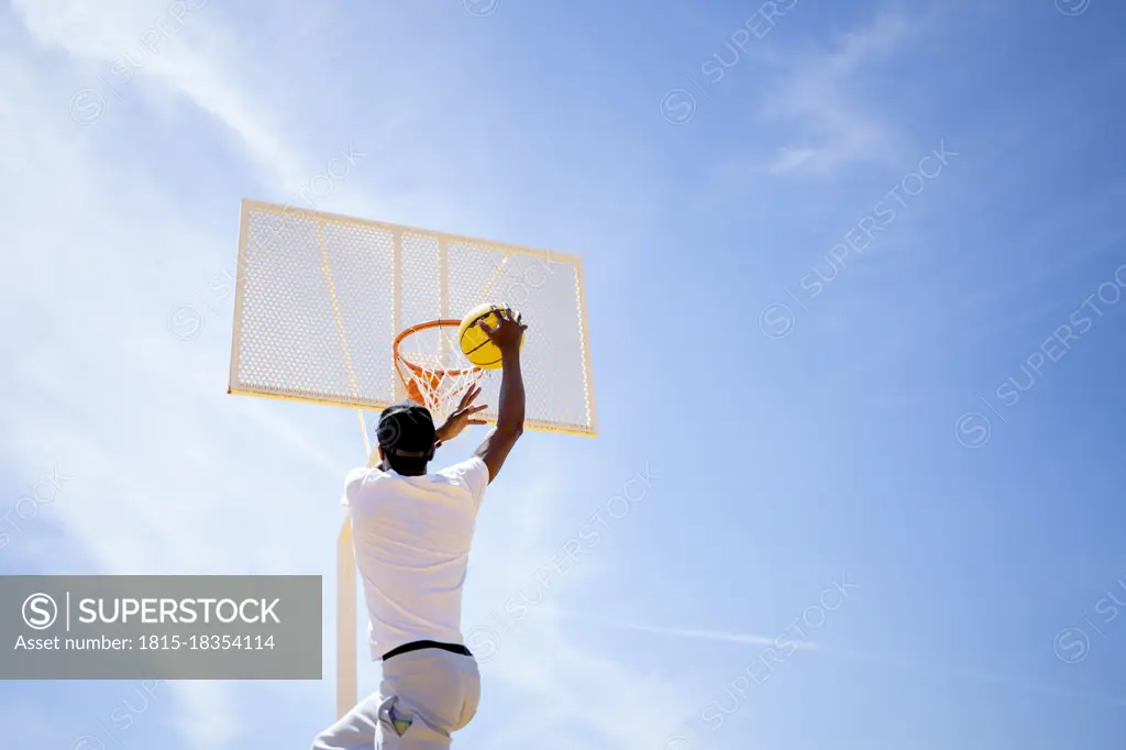 Young man playing basketball at sports court during sunny day