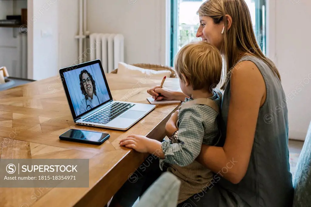 Female pediatrician assisting woman with son sitting at home