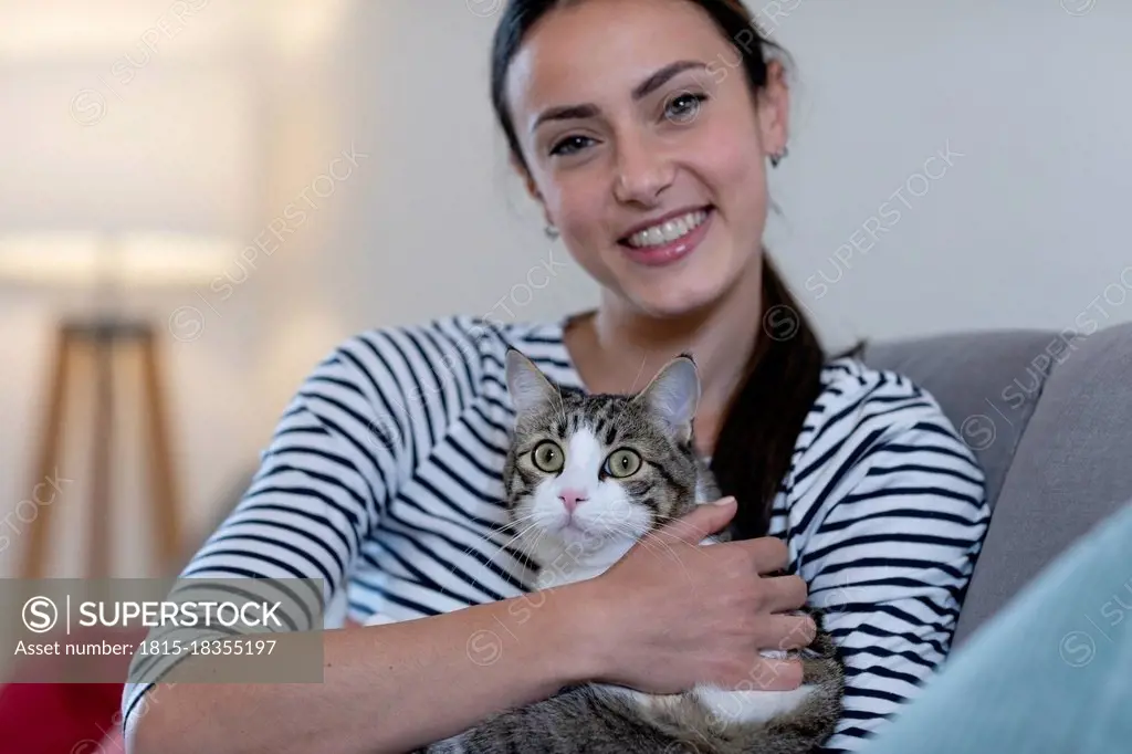 Smiling woman with tabby cat on sofa at home