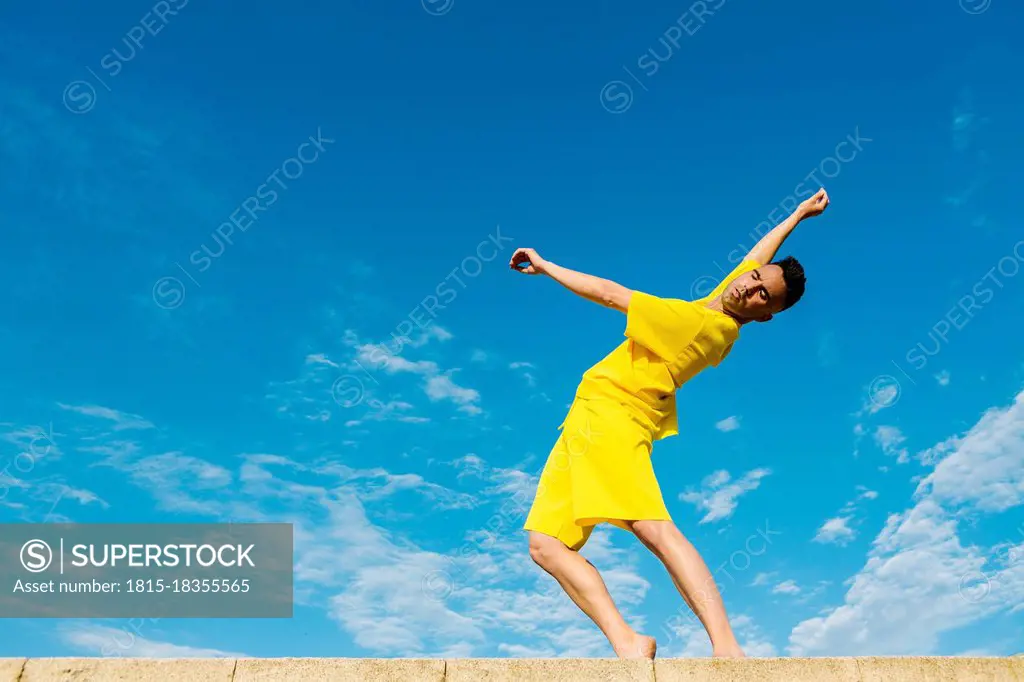 Young man dancing on retaining wall by blue sky