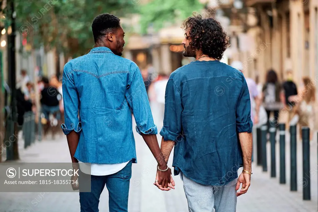 Gay couple holding hands looking at each other while walking on footpath