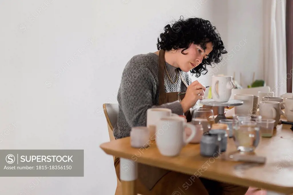 Female craftsperson painting cup while working at workshop