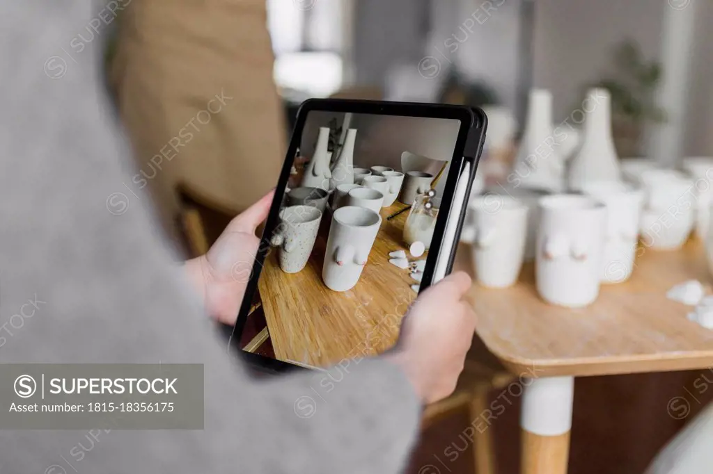 Female artist photographing art products through digital tablet at workshop