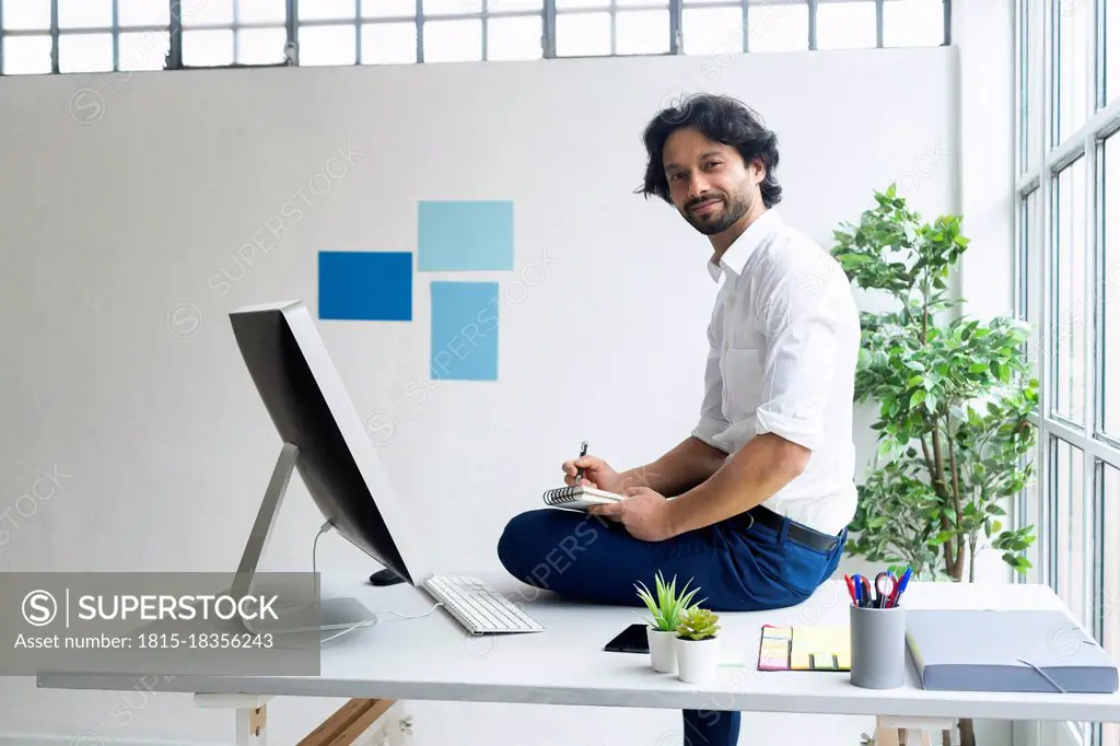 Male entrepreneur with notepad sitting on desk in office